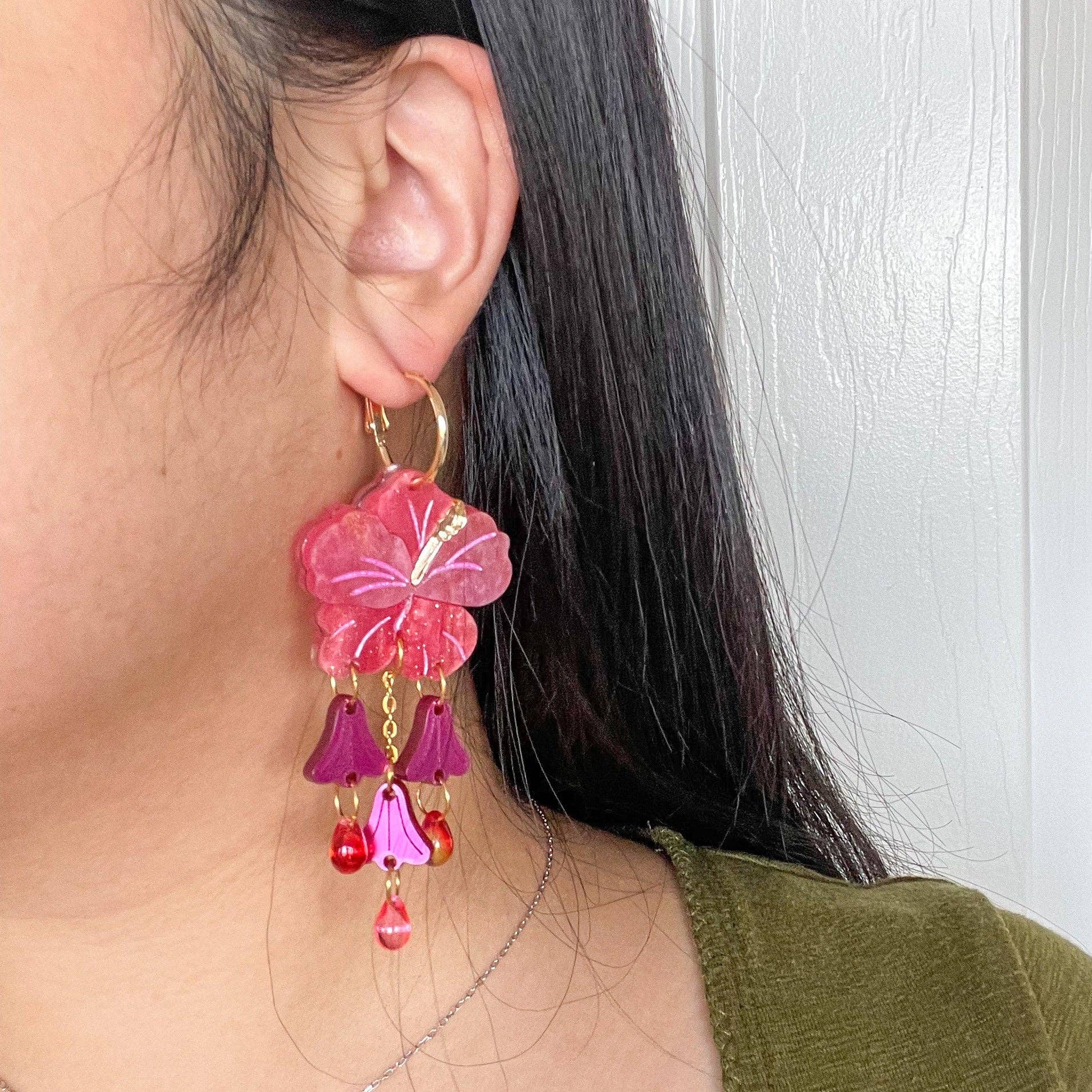 Close-up image of Hibiscus Dangle earrings by Sunnie Creative, worn by a model, showcasing the unique flower design and color details against a neutral background.