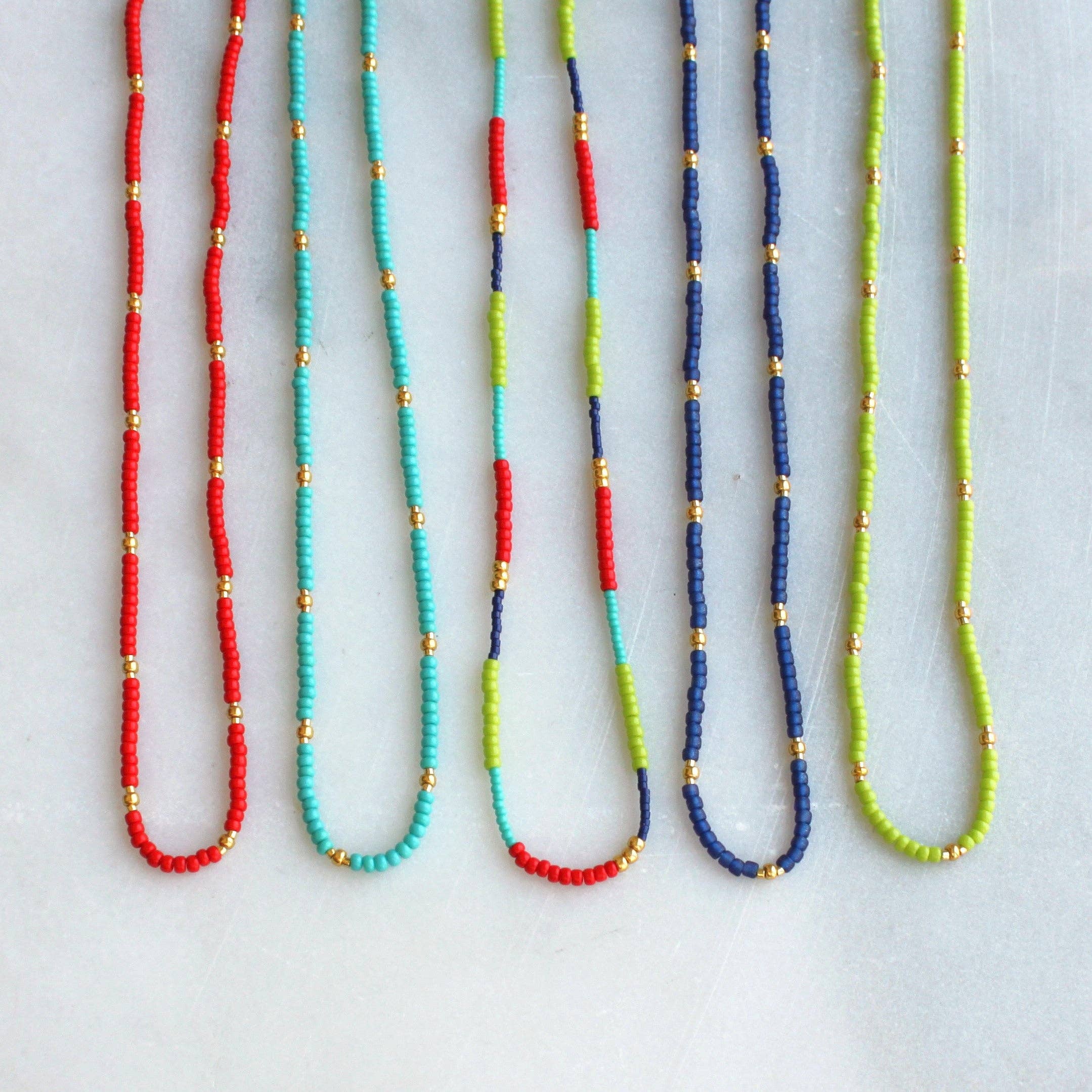 Colorful Lettie Seed Bead Necklaces by The Silver Wren, featuring vibrant seed beads in combinations of red, turquoise, navy, and green, accented with tiny gold beads, perfect for layering or wearing solo.