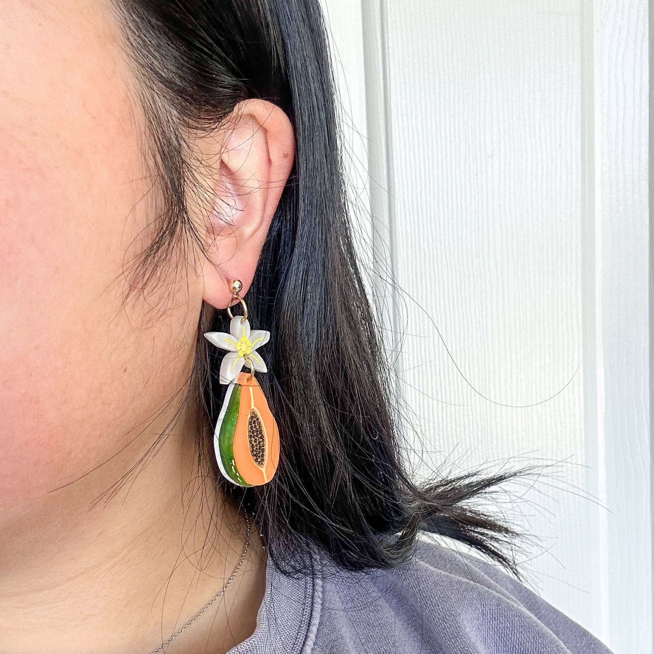A person wearing Papaya Dangle earrings by Sunnie Creative, featuring intricate details and a flower design, demonstrating comfort and style in a casual setting.