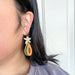 A person wearing Papaya Dangle earrings by Sunnie Creative, featuring intricate details and a flower design, demonstrating comfort and style in a casual setting.