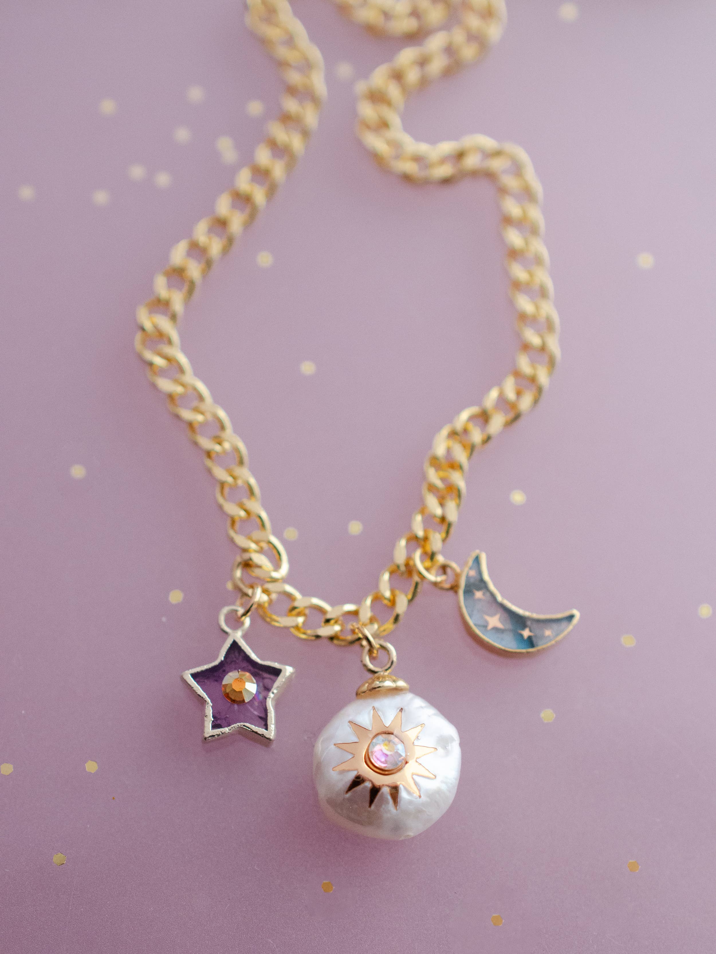 Stylish display of the Pearl and Moon Celestial Charm Necklace by Jill Makes, highlighting the unique gold-detailed charms including an amethyst star, a shining pearl sun, and a labradorite moon on a delicate chain.