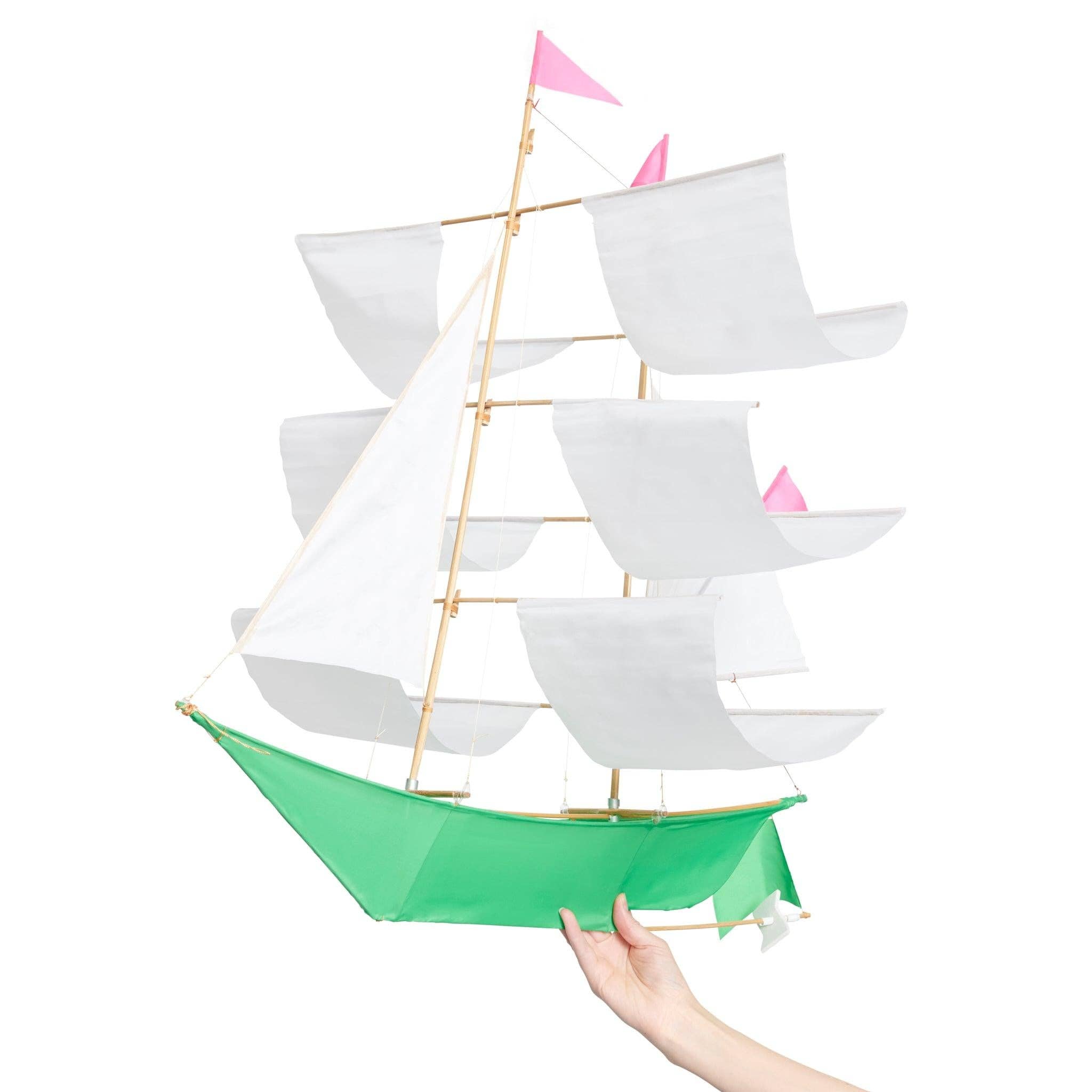 White and green Sailing Ship Kite by Haptic Lab, being held by a person, showcasing its handmade quality and elegant design.