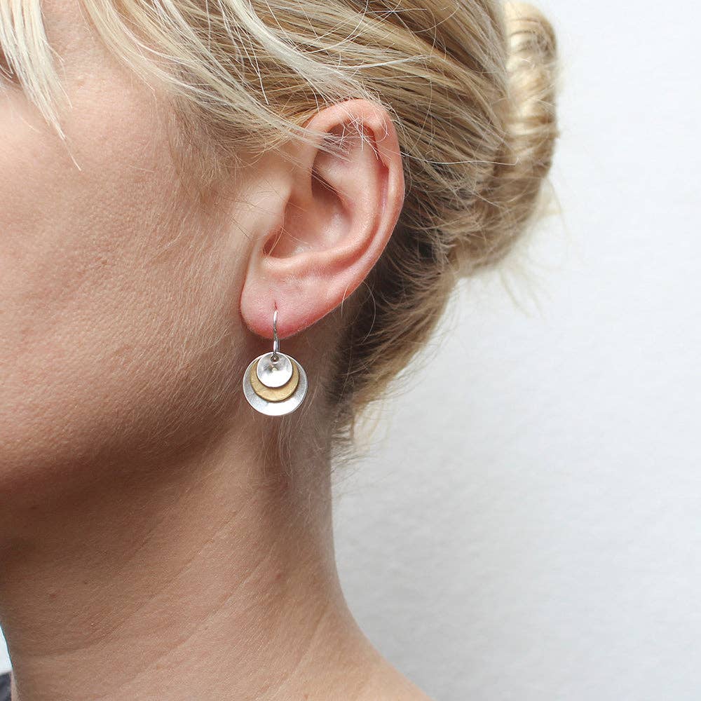 Profile view of a model wearing Three Layered Cymbals Wire Earrings by Marjorie Baer, featuring tiered brass and silver cymbals for stylish appeal.