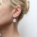 Profile view of a model wearing Three Layered Cymbals Wire Earrings by Marjorie Baer, featuring tiered brass and silver cymbals for stylish appeal.