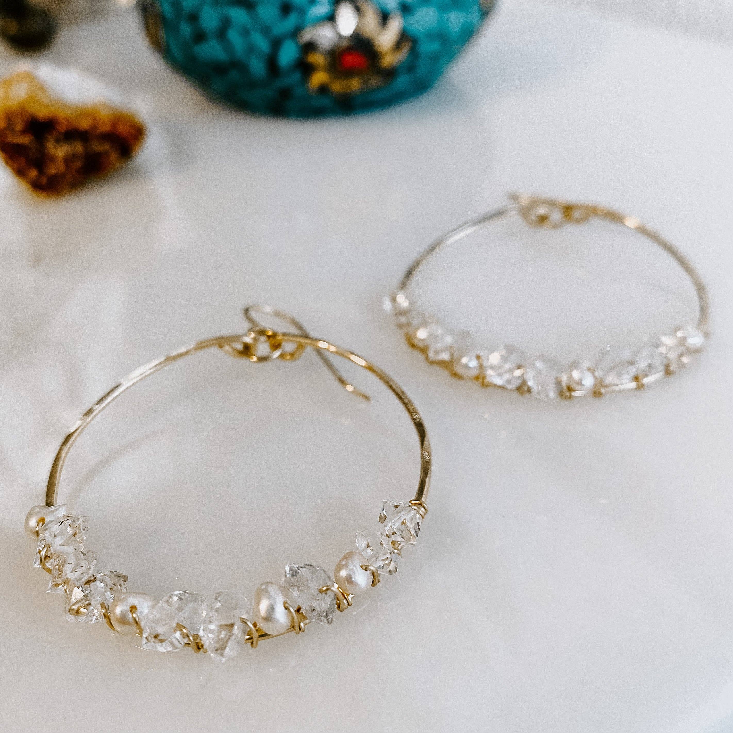 Stylish display of Everly Herkimer Diamond and Pearl Hoop Earrings from Derive Jewelry, highlighting the combination of sparkling gemstones and pearls on a sleek surface.