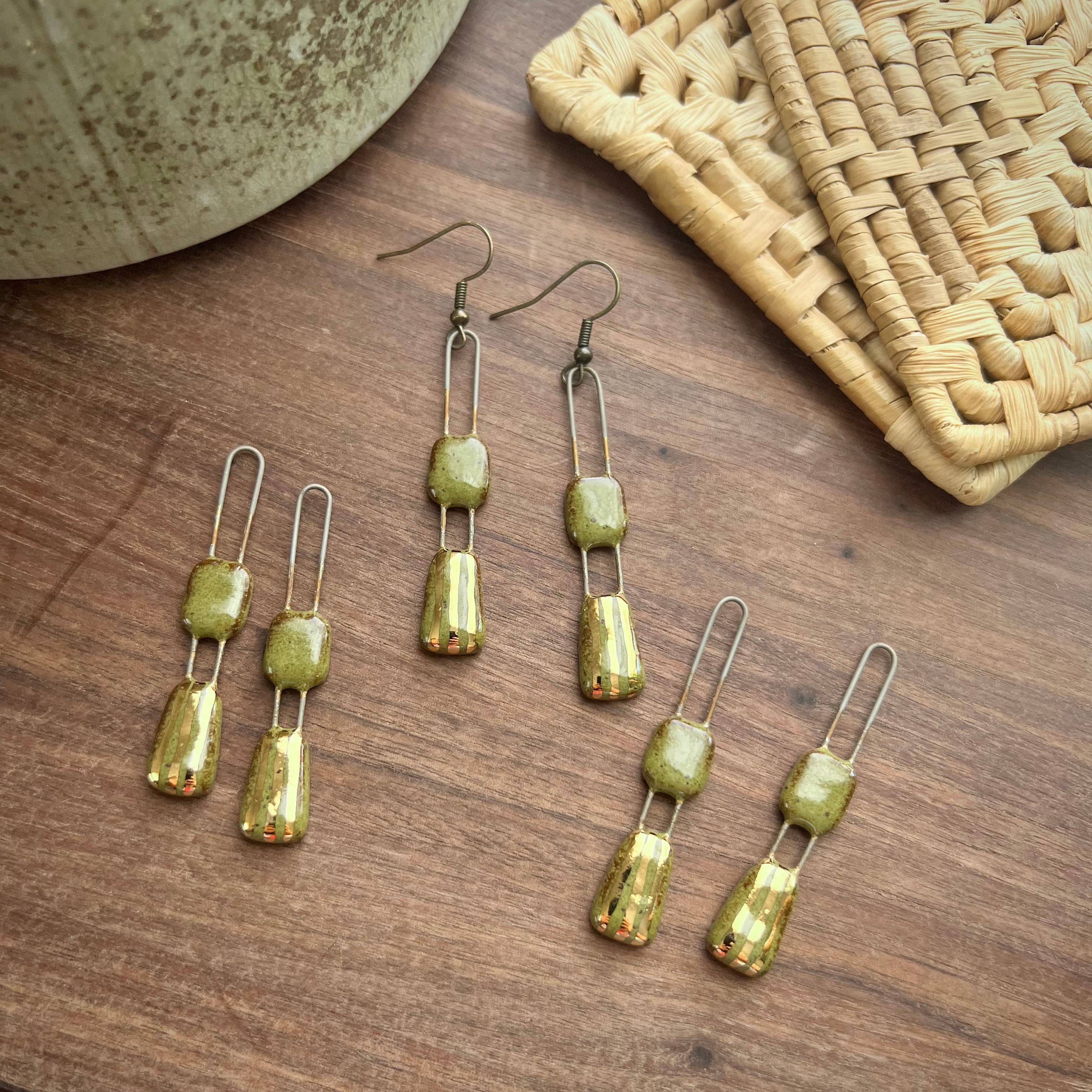 Multiple pairs of Speckled Olive Two Piece Gold Lined Earrings by The Artifact House on a wooden surface, with a textured bowl and woven basket.