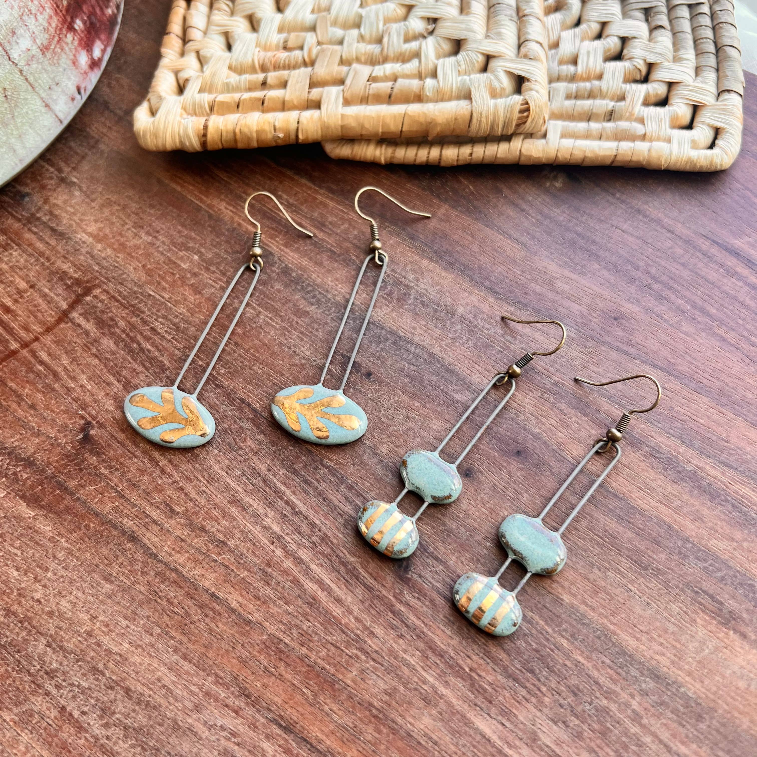 A variety of turquoise double bubble and leaf design gold striped ceramic earrings by The Artifact House, artfully displayed with rustic elements.