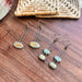 A variety of turquoise double bubble and leaf design gold striped ceramic earrings by The Artifact House, artfully displayed with rustic elements.