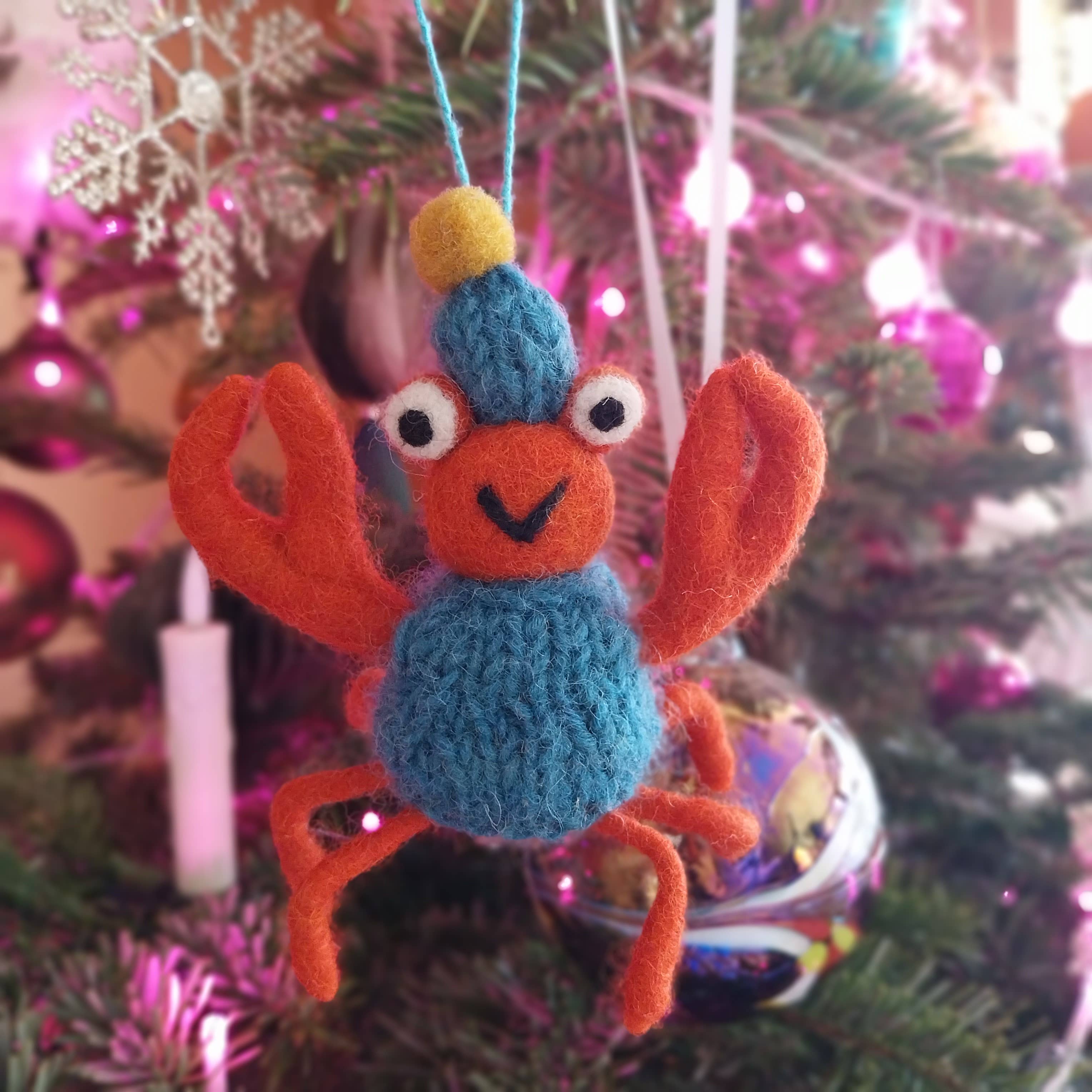 Felt crab ornament hanging on a Christmas tree with colorful lights in the background