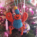 Felt crab ornament hanging on a Christmas tree with colorful lights in the background