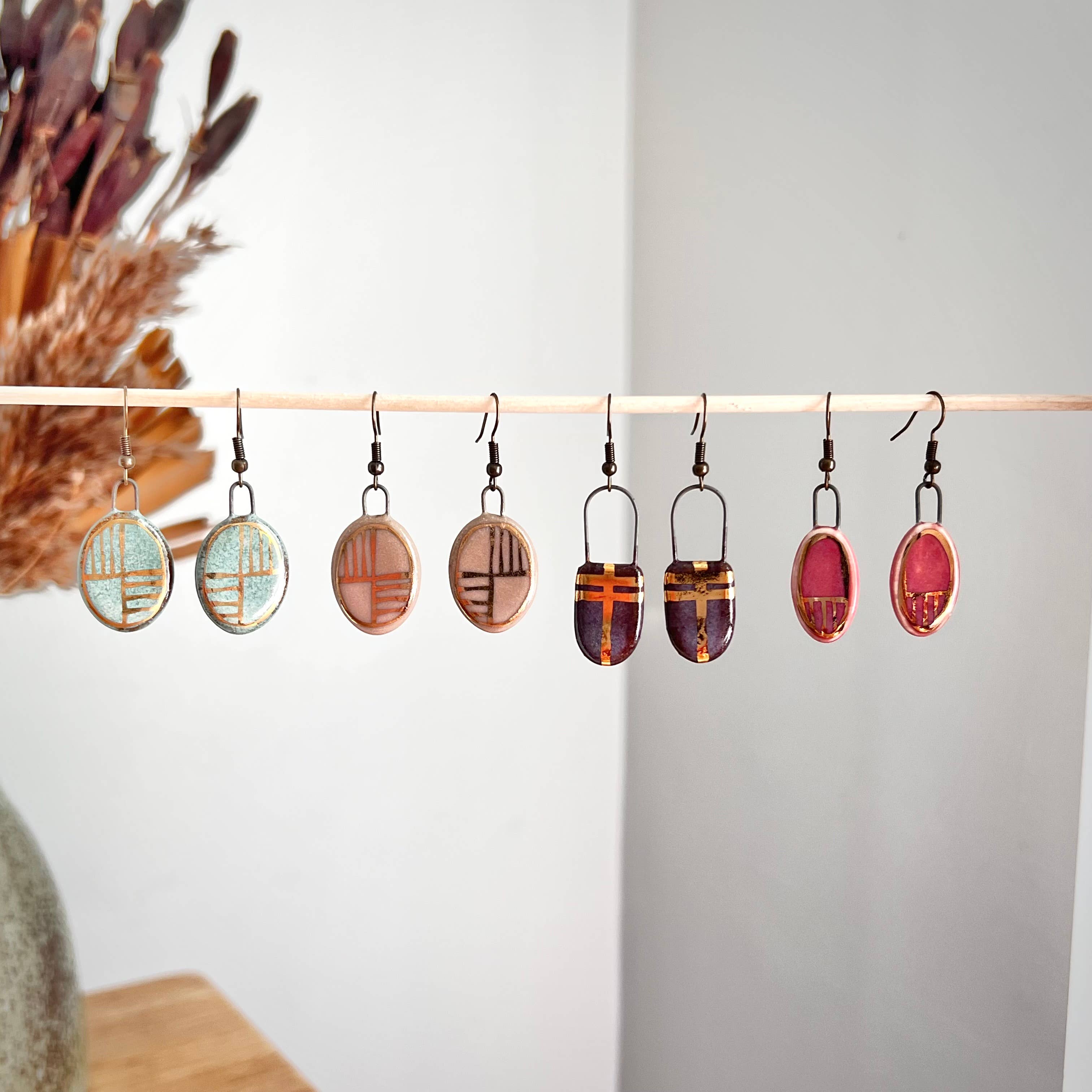 A display of handmade turquoise oval earrings with gold checkered lines by The Artifact House, showcasing their unique ceramic designs. Each pair features a blend of colors and patterns, emphasizing the elegant and artisanal qualities of the jewelry.
