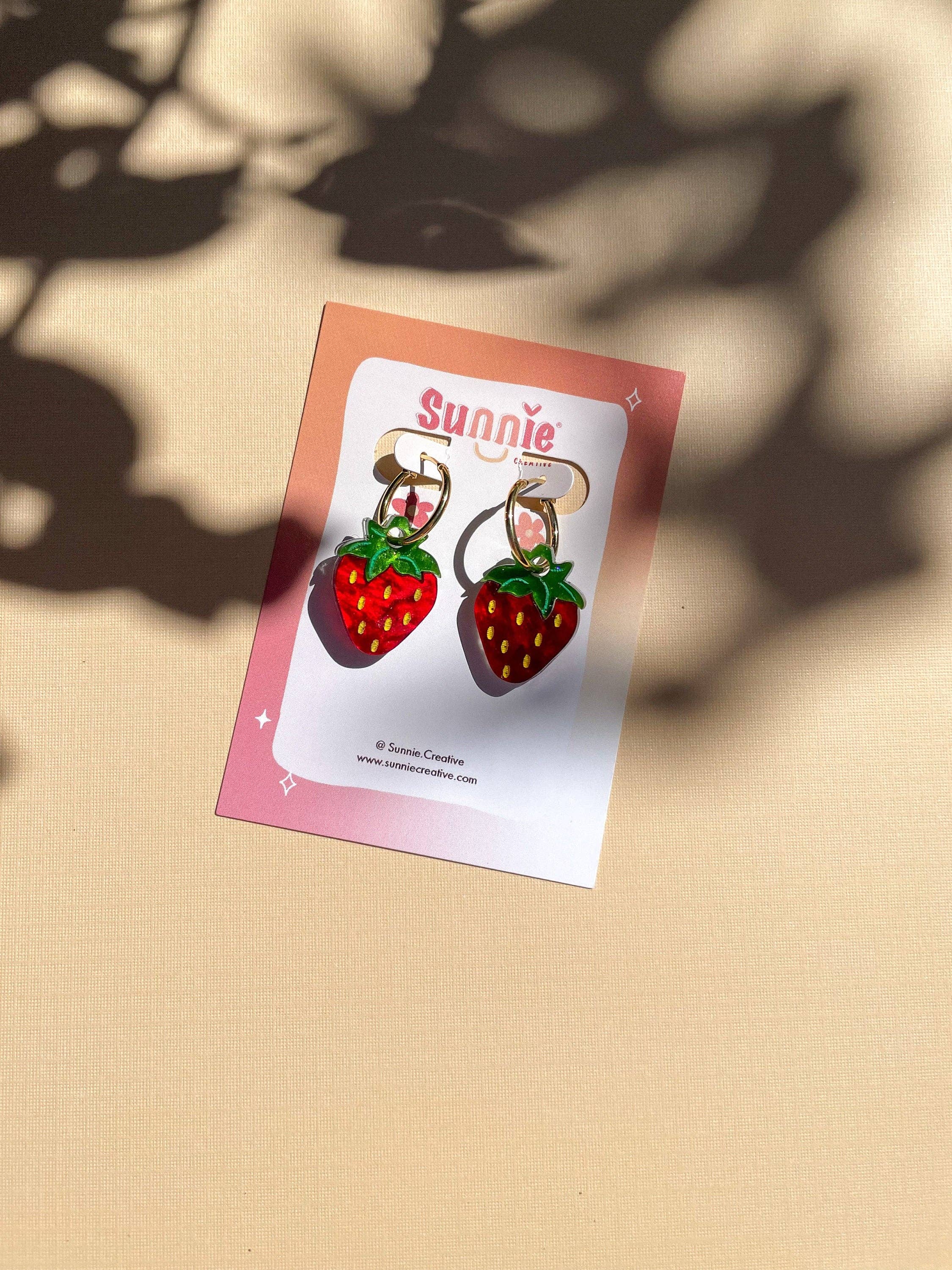 Mini Strawberry Acrylic Dangle Earrings by Sunnie Creative displayed on a branded card against a soft background with shadows.