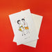 Kris Goto Card Collection featuring a whimsical illustration of a couple, with the woman in a floral dress and the man in shorts, set against a vibrant red background. Perfect for greeting card lovers.