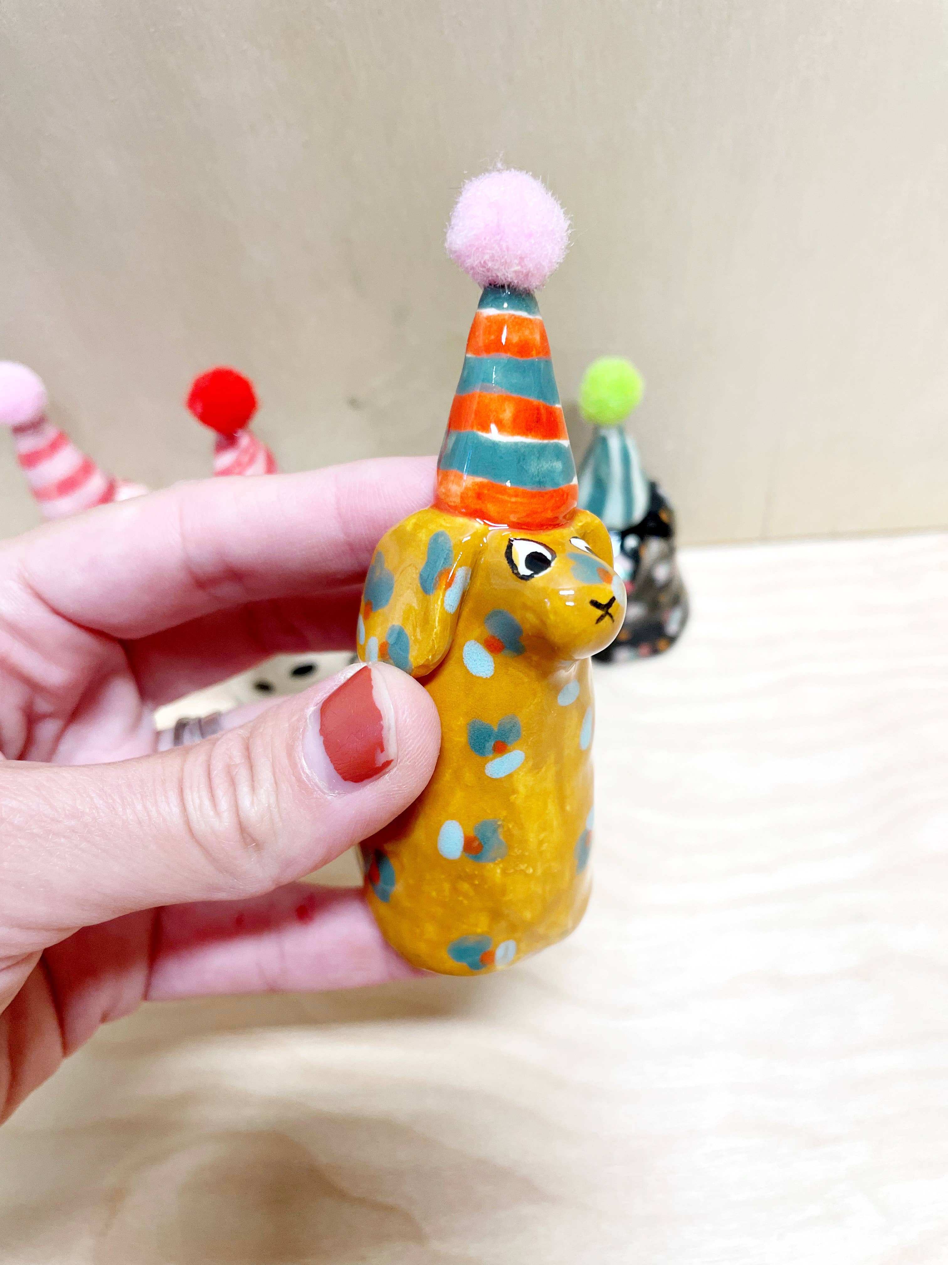 Vibrant mini party dog in yellow with blue flower patterns and a striped orange party hat, crafted by Bianca Rae. Ideal for adding whimsy to 'Party Minis! Mini Party Dogs in Party Hats.'