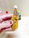 Vibrant mini party dog in yellow with blue flower patterns and a striped orange party hat, crafted by Bianca Rae. Ideal for adding whimsy to 'Party Minis! Mini Party Dogs in Party Hats.'