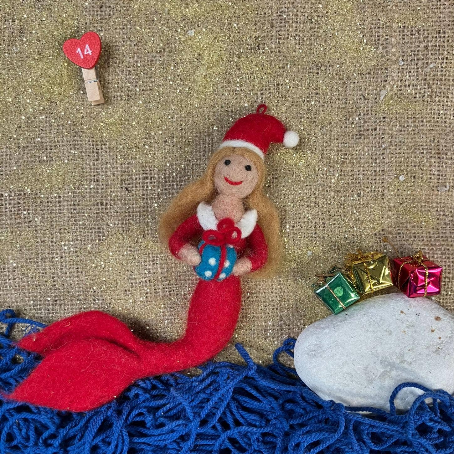 felt Mermaid ornament waring Santa hat with Christmas presents on a textured background