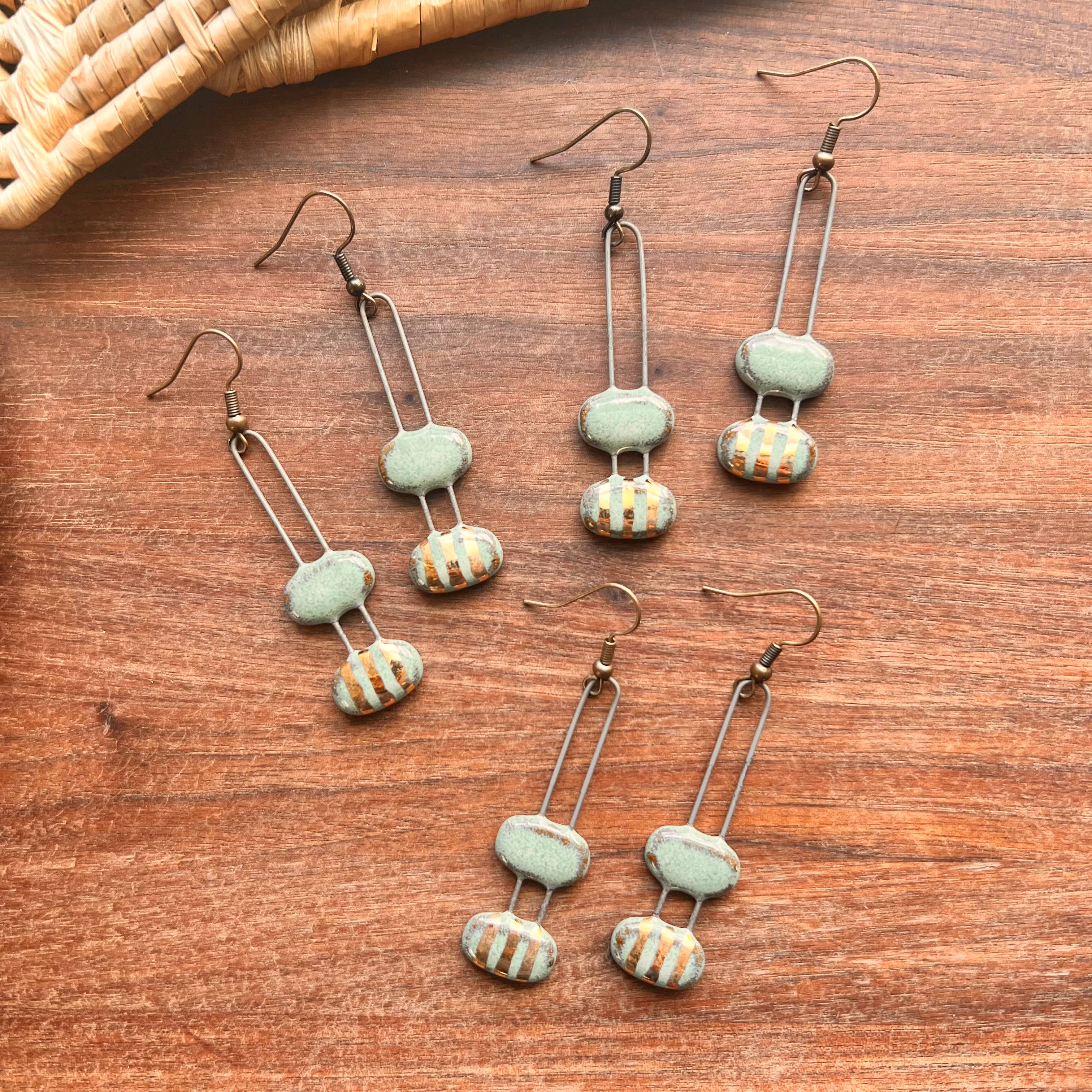 A collection of turquoise double bubble gold striped ceramic earrings by The Artifact House, arranged in a stylish layout on a wooden surface.