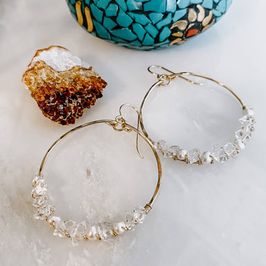 Stylish display of Everly Herkimer Diamond and Pearl Hoop Earrings by Derive Jewelry next to a turquoise decor, highlighting the elegant design with Herkimer diamonds and pearls.