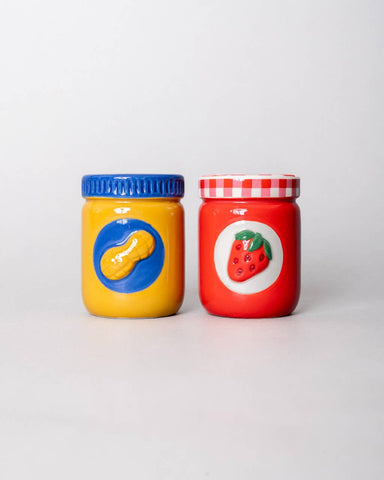 Two colorful ceramic jars, one yellow and blue lid with peanut and one red with a strawberry
