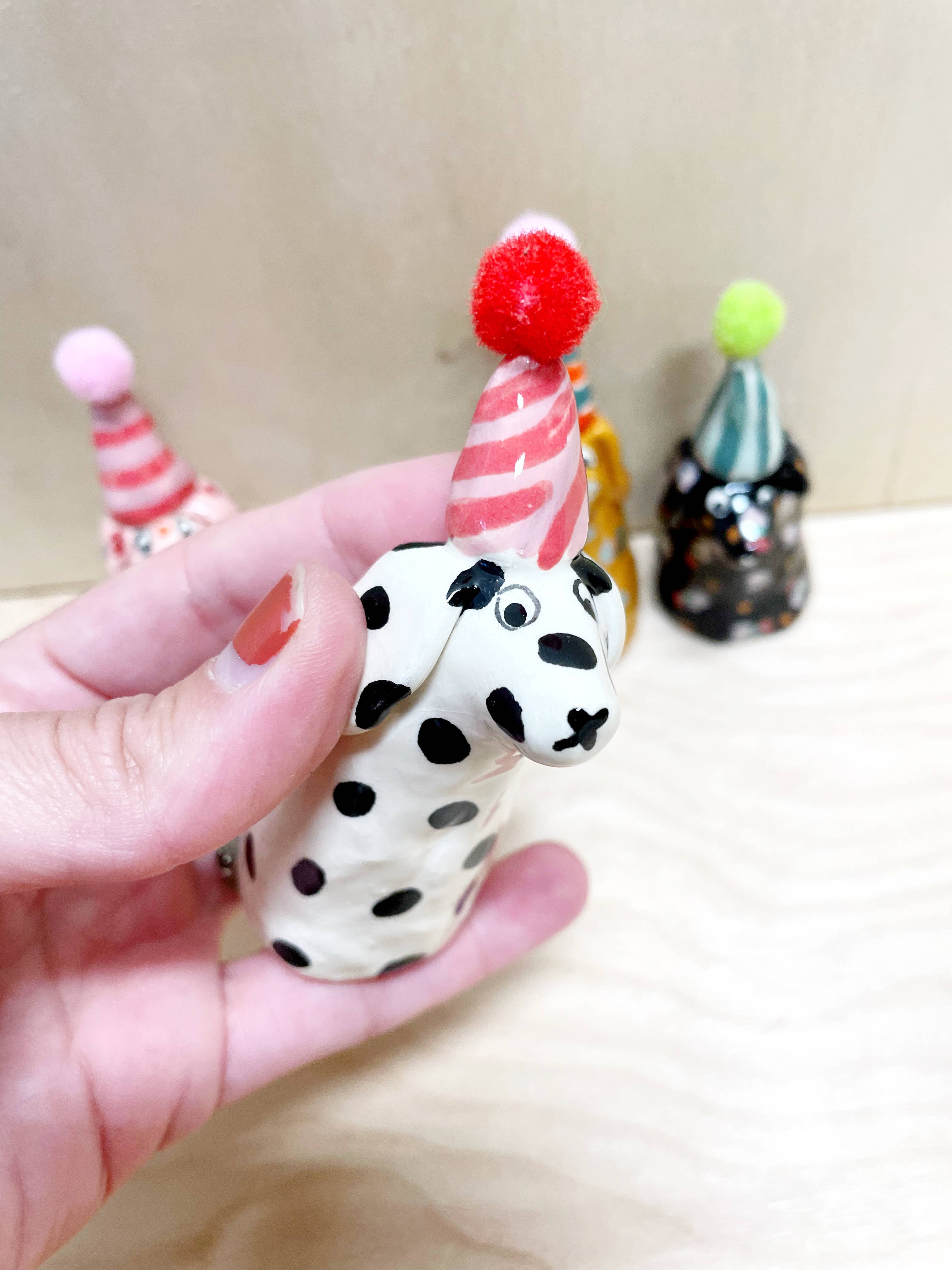 Charming mini party dog with a white coat and black spots, wearing a red and white striped party hat, designed by Bianca Rae. Great addition to 'Party Minis! Mini Party Dogs in Party Hats.'