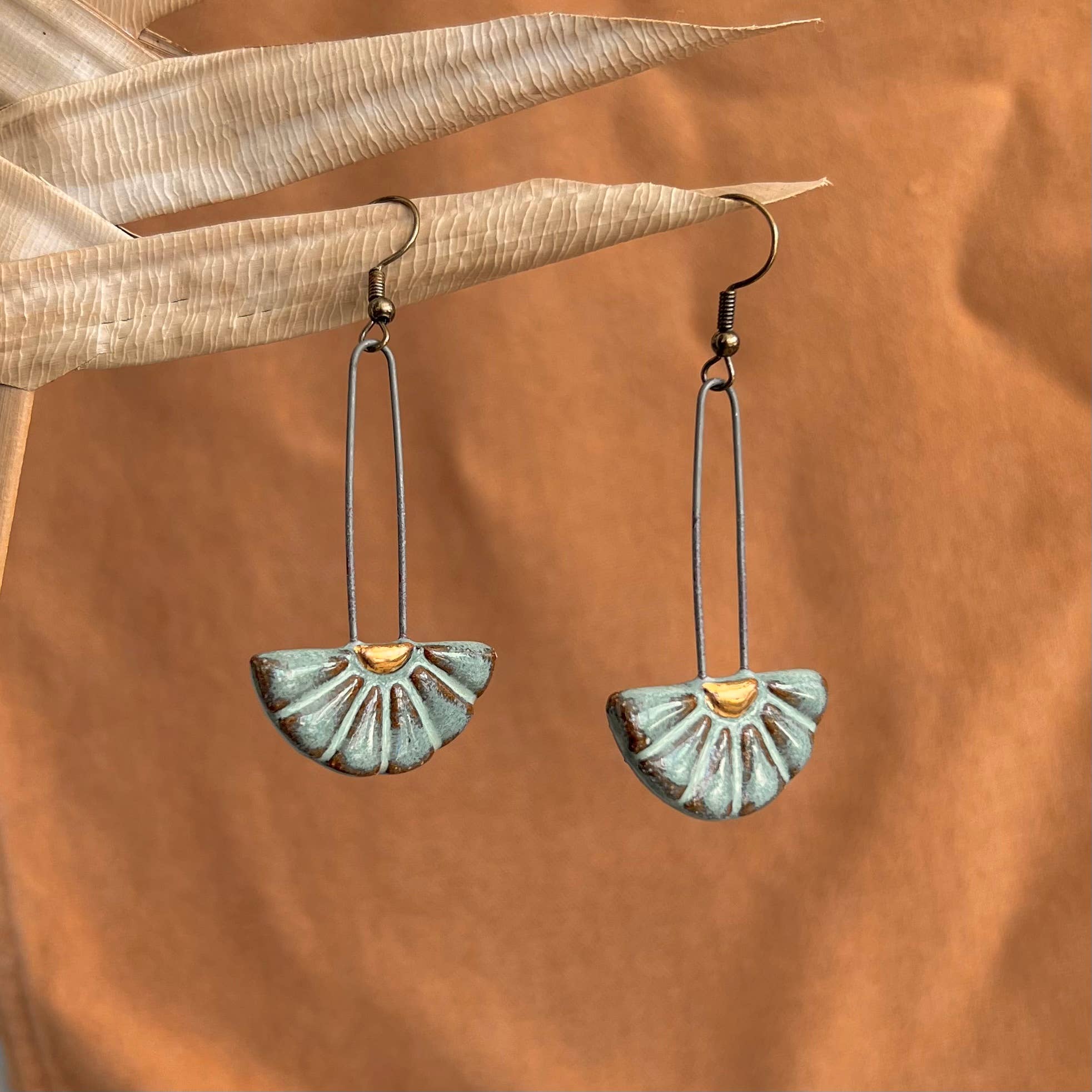 Close-up view of Turquoise Sun Burst Ceramic Earrings by The Artifact House, highlighting the intricate sun burst patterns against a warm earthy background.