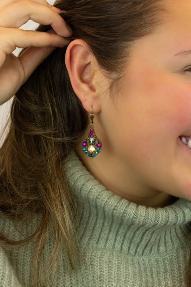 Close-up of a person wearing a colorful gemstone earring with a green sweater.