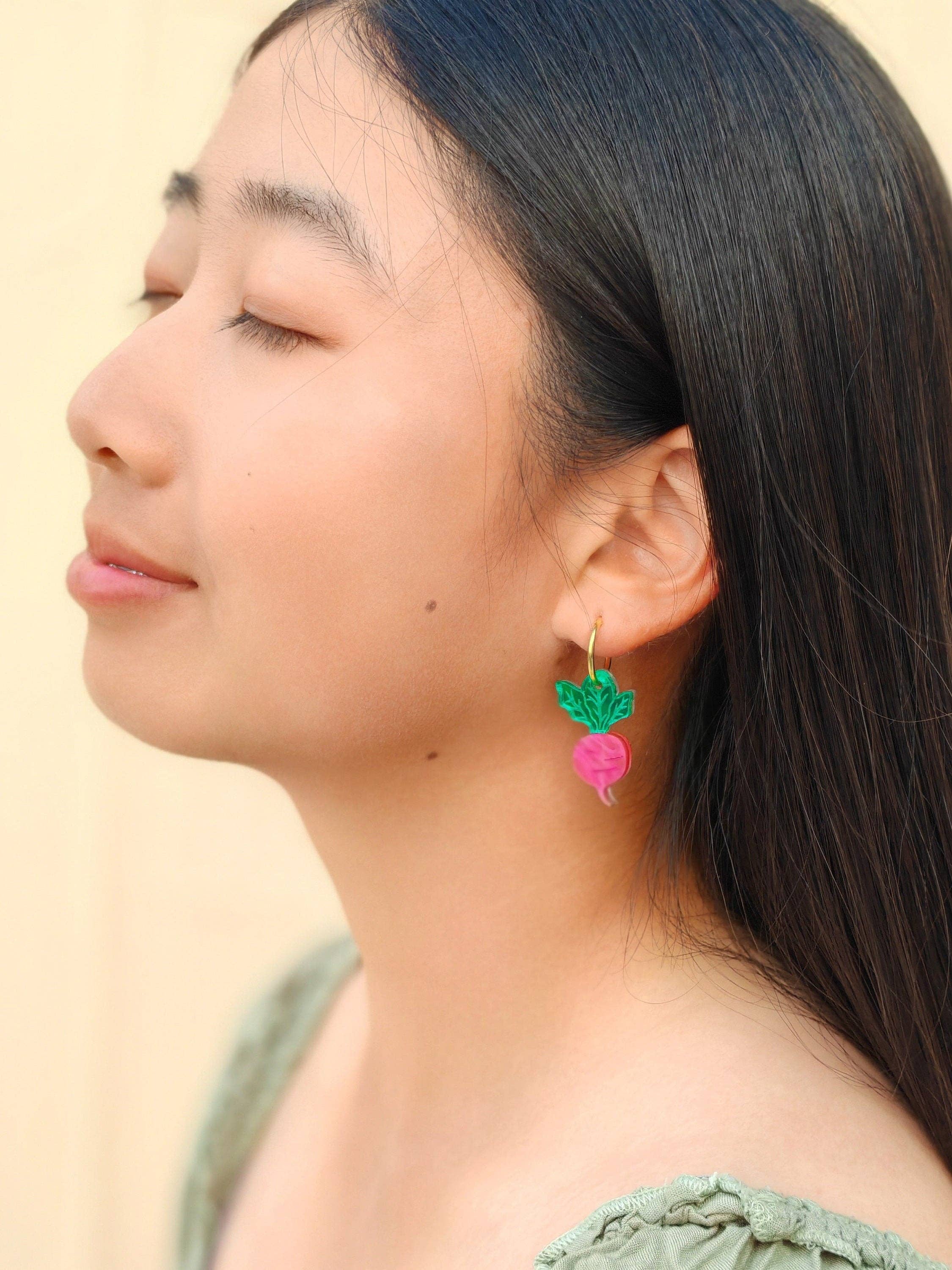 Model wearing Mini Radish Dangle earrings by Sunnie Creative, showcasing the playful pink radish design with green leaves, styled in a casual setting.