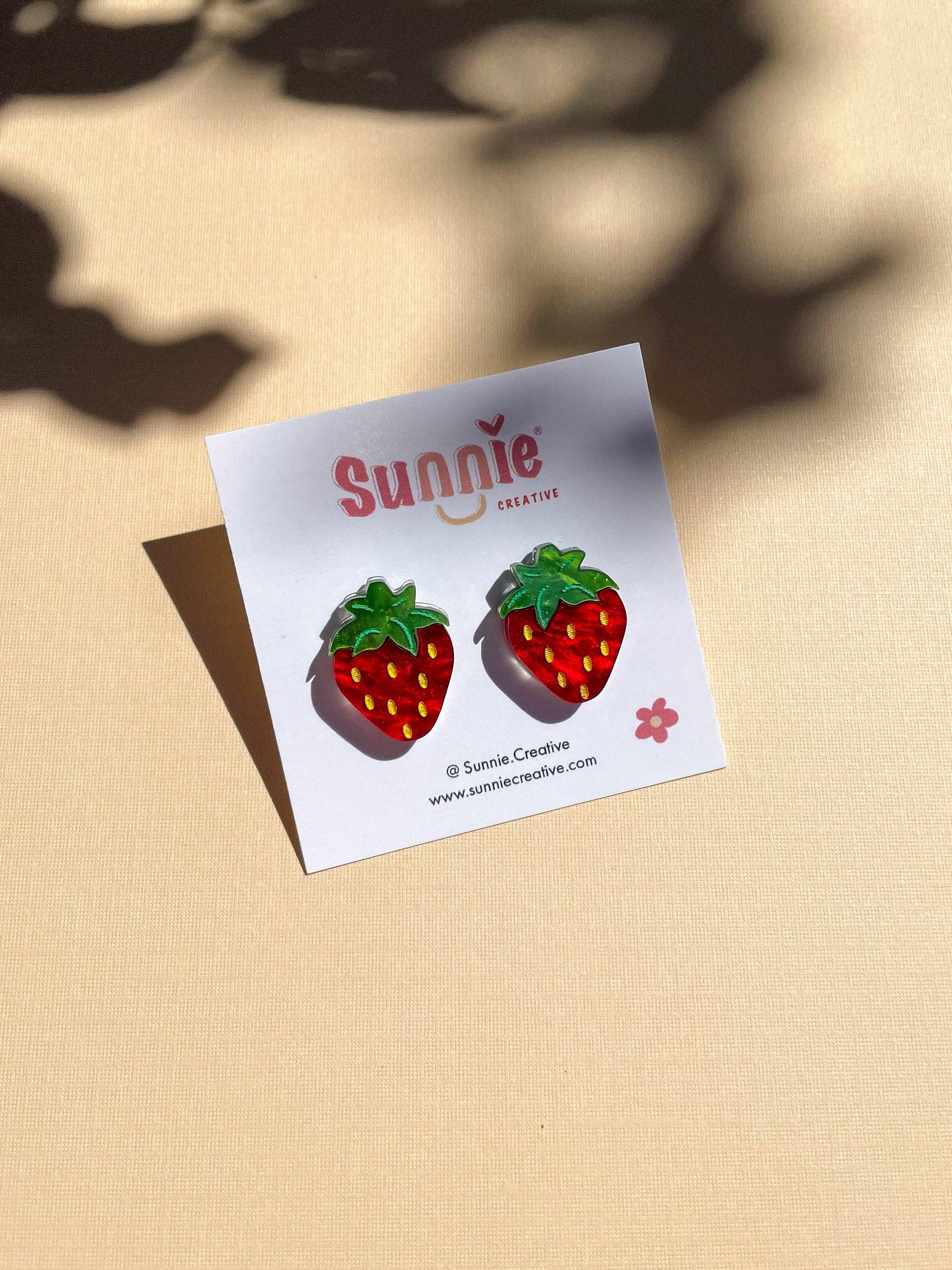 Mini Strawberry Acrylic Dangle Earrings by Sunnie Creative on a branded card, featuring vibrant colors and a playful design against a subtle background.