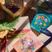 Various Bespoke Blooms seed ball kits by Modern Sprout arranged artistically among gift-wrapped items and natural decorations, showcasing spring-to-fall wildflowers.