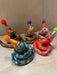 A colorful assortment of Itty Bitty Party Snake Sculptures by Bianca Rae, featuring whimsical designs with party hats topped with pom poms. Each snake is unique in color and style, perfect for cake toppers or charming decor.