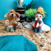 Felt hippo and dog ornaments on a sandy surface with a blue background