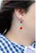 Side view of Heart Charm Earrings by Jill Makes, featuring a detailed look at the red heart charms and bead arrangement, worn by a model against a background of patterned clothing.