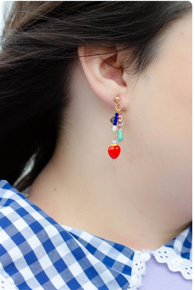Side view of Heart Charm Earrings by Jill Makes, featuring a detailed look at the red heart charms and bead arrangement, worn by a model against a background of patterned clothing.