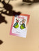 Mini Pear Dangle earrings by Sunnie Creative displayed on a stylish card, featuring a unique design of green acrylic pears with leaf accents, highlighted with natural lighting.