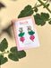 Mini Radish Dangle earrings displayed on a card by Sunnie Creative, featuring vibrant pink radish designs with green leaves, perfect for adding a playful touch to your outfit.