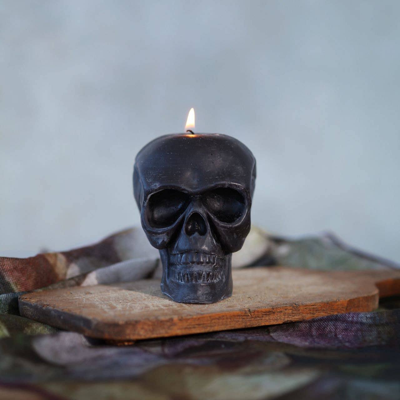 Black skull-shaped candle with a flame on a wooden surface