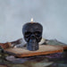 Black skull-shaped candle with a flame on a wooden surface