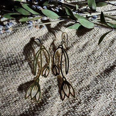 Snowdrop Stained Glass Resin Earrings by Wild Lupine Folkcraft, showcasing a unique and colorful handmade design against a natural backdrop of greenery.