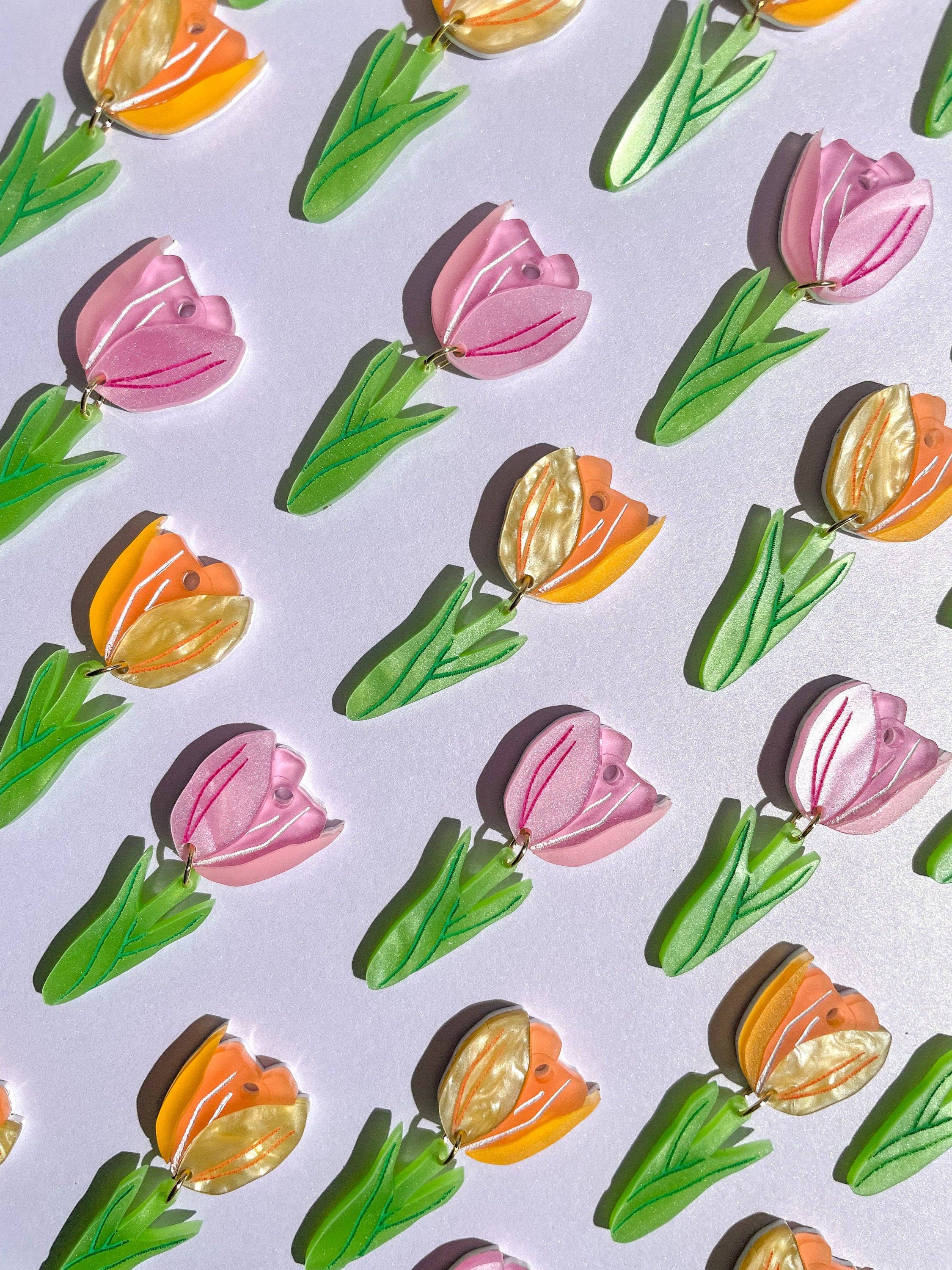 A vibrant arrangement of Spring Tulip earrings by Sunnie Creative, featuring multiple handmade designs of tulip motifs in pink, orange, and green.