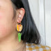 A person wearing orange and green Spring Tulip earrings by Sunnie Creative, showcasing the playful tulip design and bright colors for spring fashion.