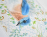 Close-up image of a bluebird fine art print by Emily Uchytil, highlighting detailed feathers and floral designs in the background, suitable for nature lovers.