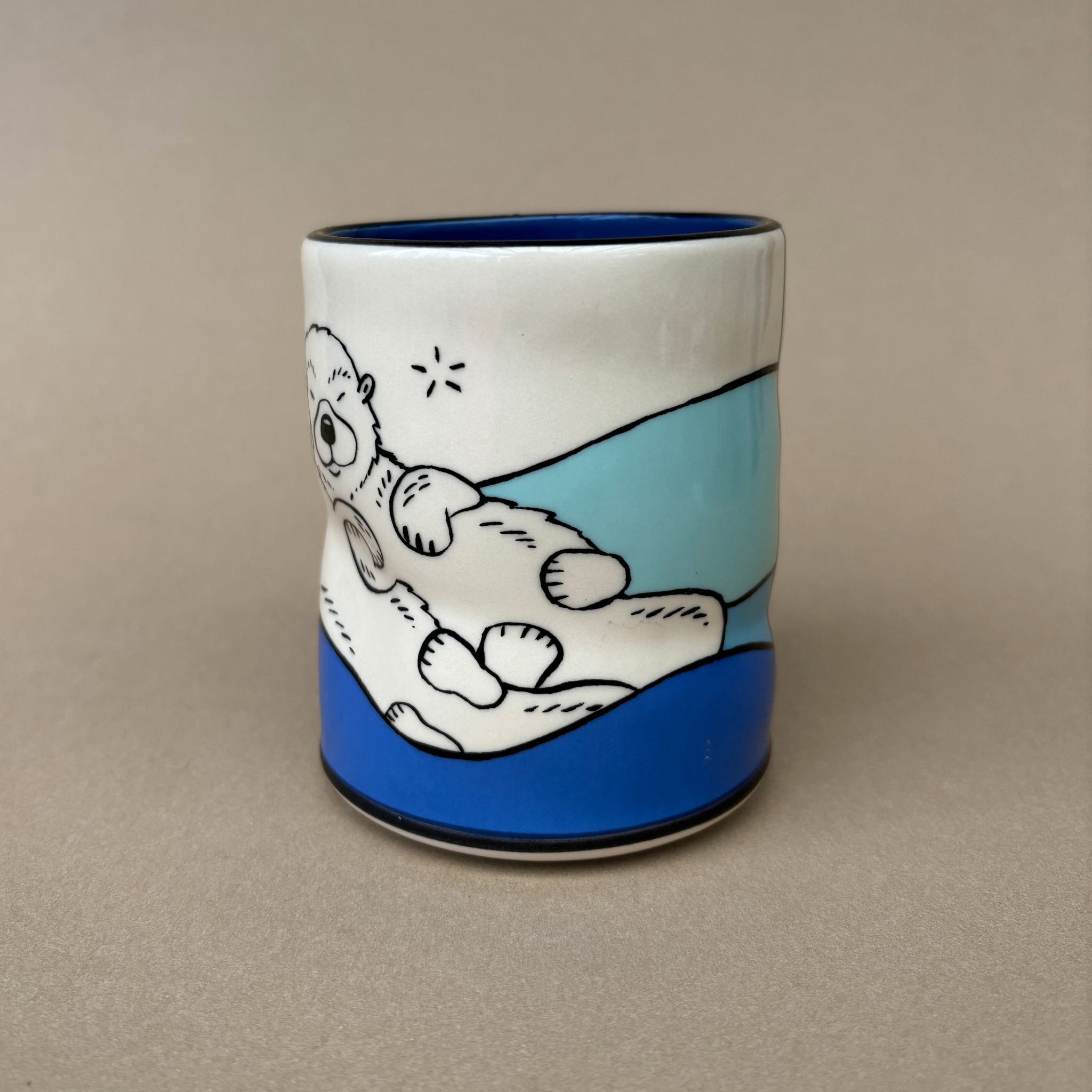 Lucky Otter Cup by The Bowl Maker, featuring a playful design of a relaxed otter on a colorful background, ideal for enjoying beverages. Large size, dishwasher safe, and art on all sides.