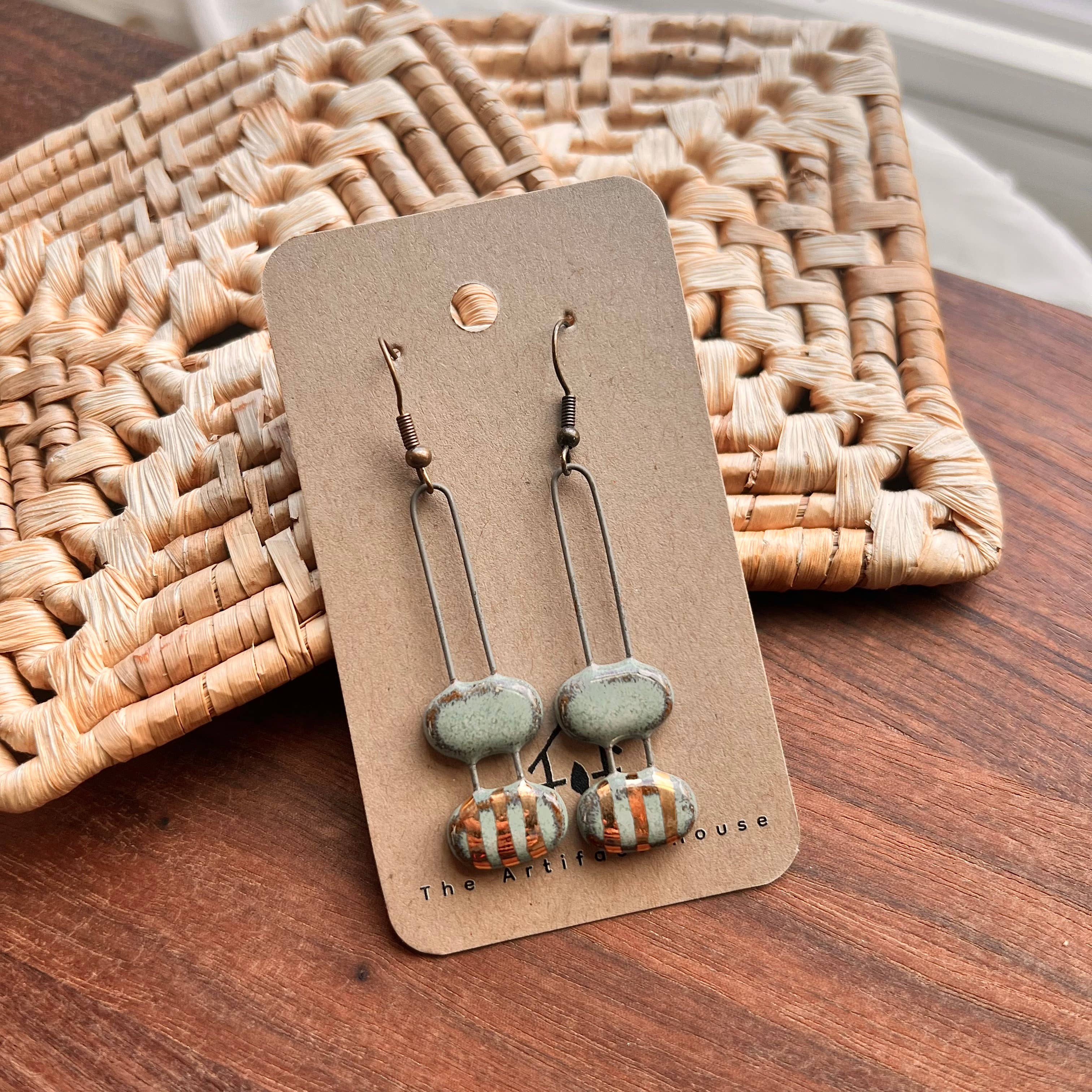Turquoise Double Bubble Gold Striped Ceramic Earrings by The Artifact House displayed on a packaging card, featuring rustic woven decor in the background.