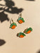 Mini Orange Dangle earrings by Sunnie Creative, featuring vibrant orange fruit designs with green leaves, displayed against a soft neutral background.