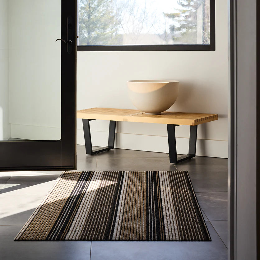 Chilewich Pleat Stripe Shag Mat - Oyster next to a modern bench