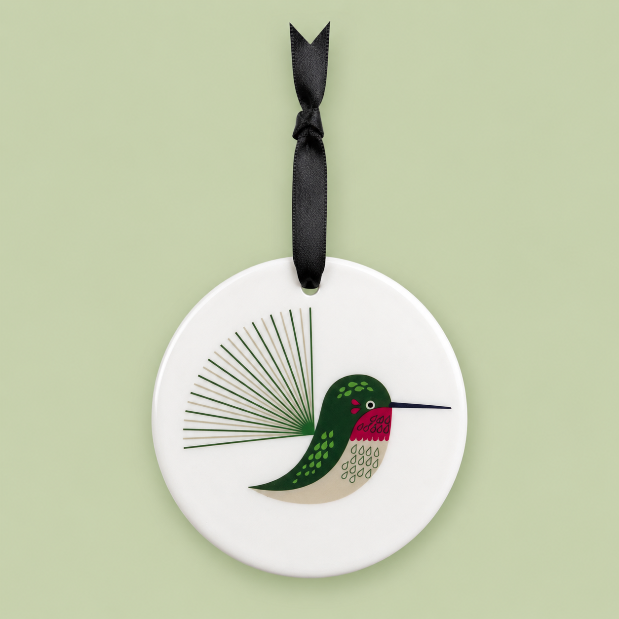 Round ceramic ornament with a hummingbird design on a light green background
