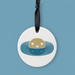 Round white ceramic tag with a brown bear illustration in water, hanging on a black ribbon against a blue background.