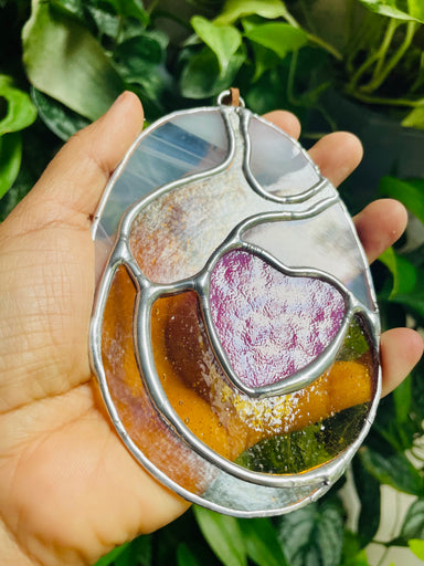 Handheld glass art piece inspired by nature, featuring vibrant colors and heart shapes, created by stained glass artist Luz Estrella for Hearts for the Arts titled 'Banana Slug Love'.