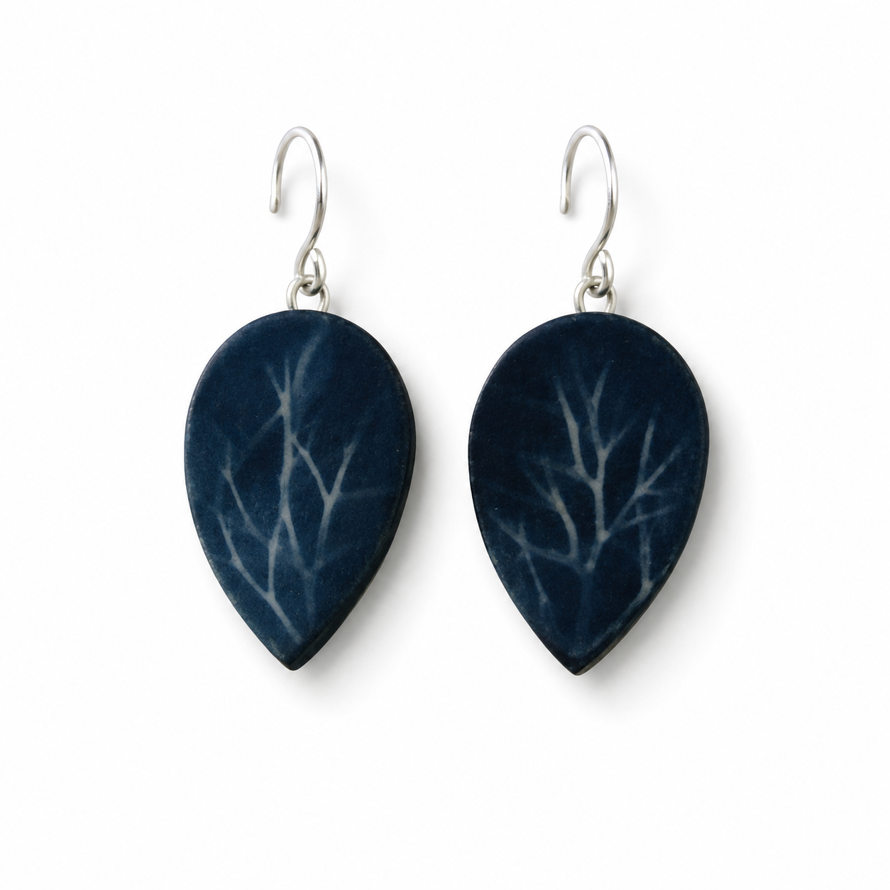 A pair of teardrop-shaped drop earrings with a dark navy blue background and a light gray branch or tree-like pattern, suspended from silver fishhook wires on a plain white background.