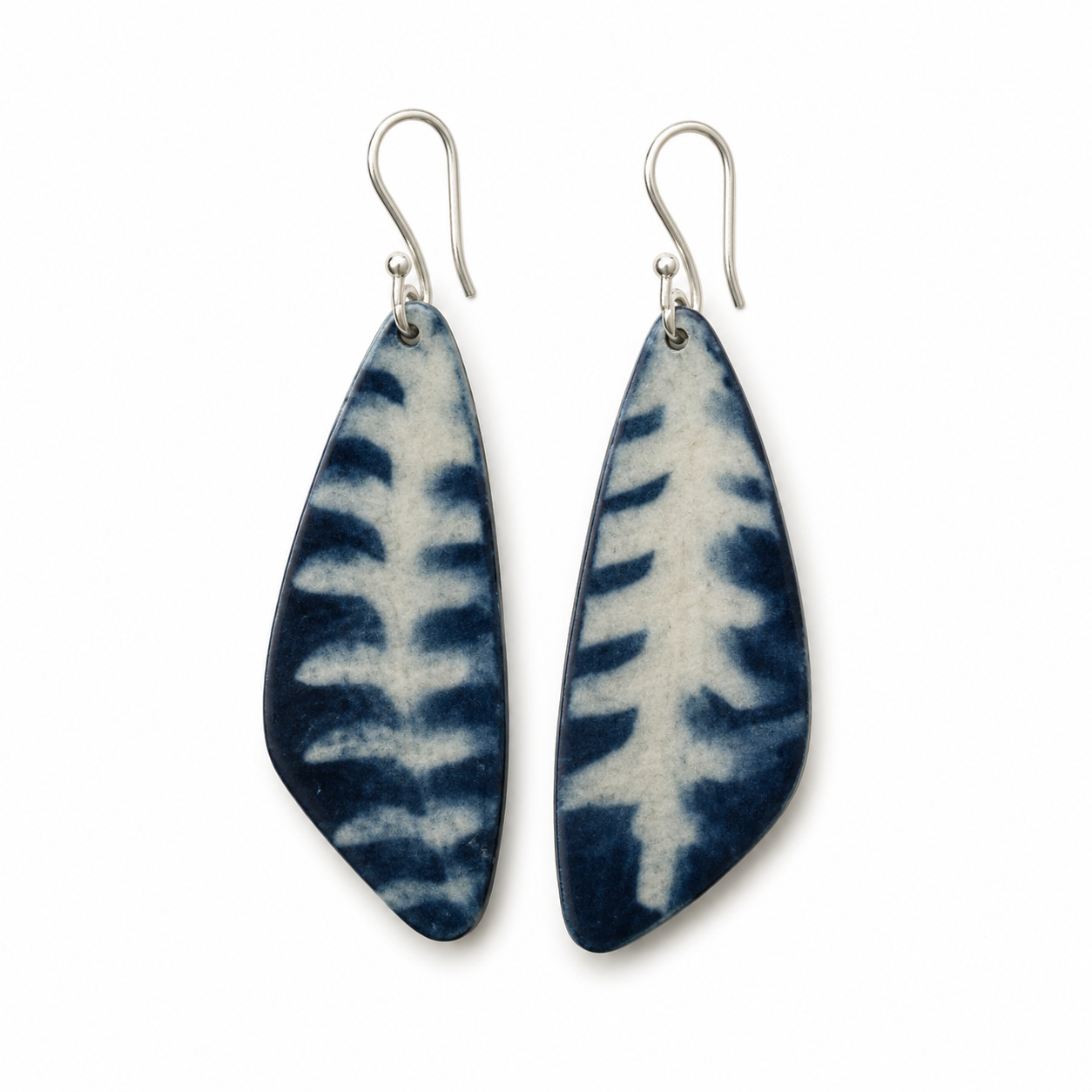 A pair of teardrop-shaped drop earrings with a dark blue and white shibori tie-dye pattern, suspended from silver fishhook wires, shown against a plain white background.